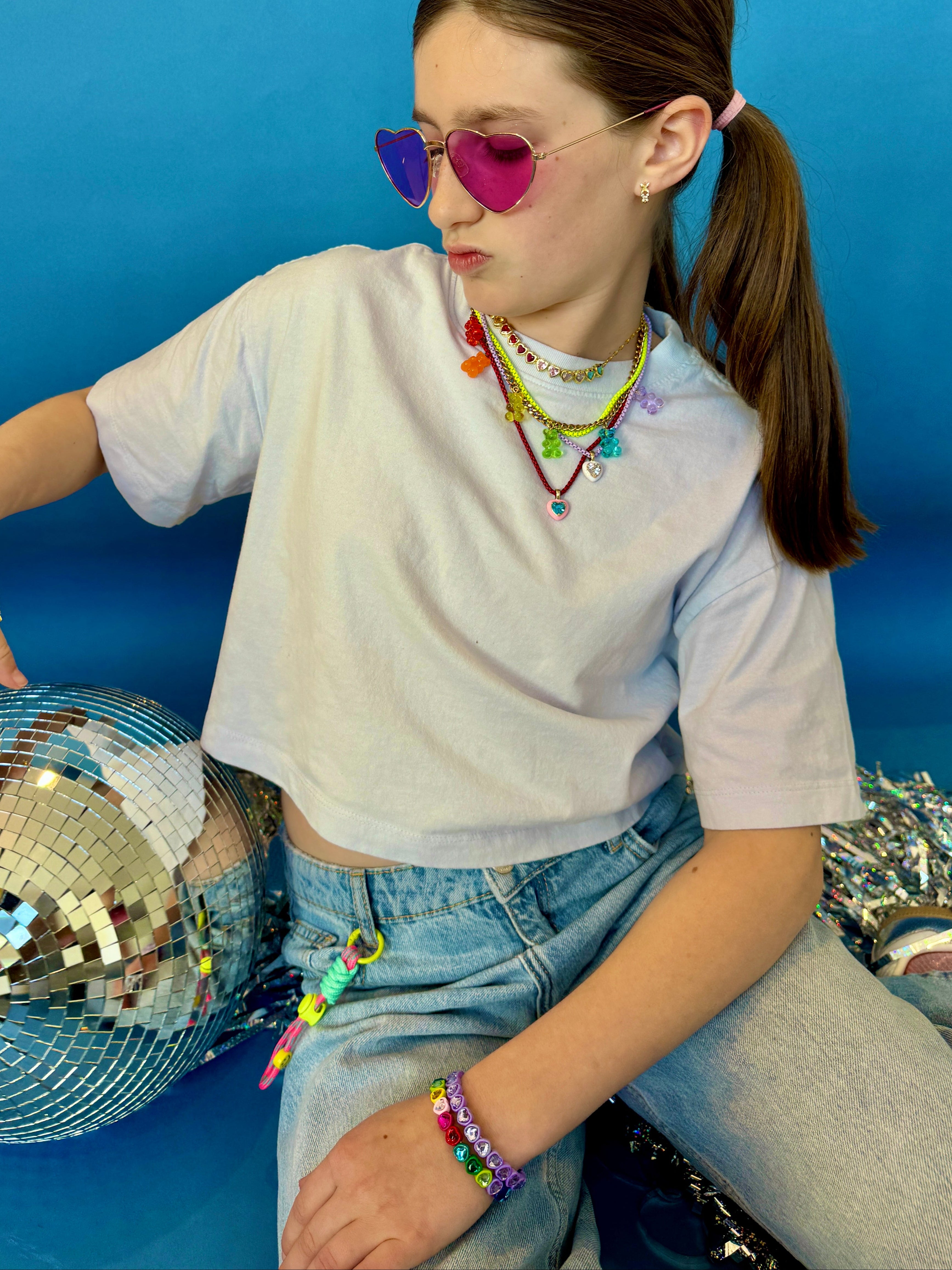 Person wearing colorful accessories and sitting on a blue background with disco balls.
