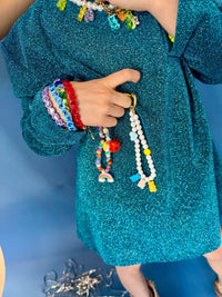 Person wearing colorful bracelets and holding a beaded necklace against a blue background