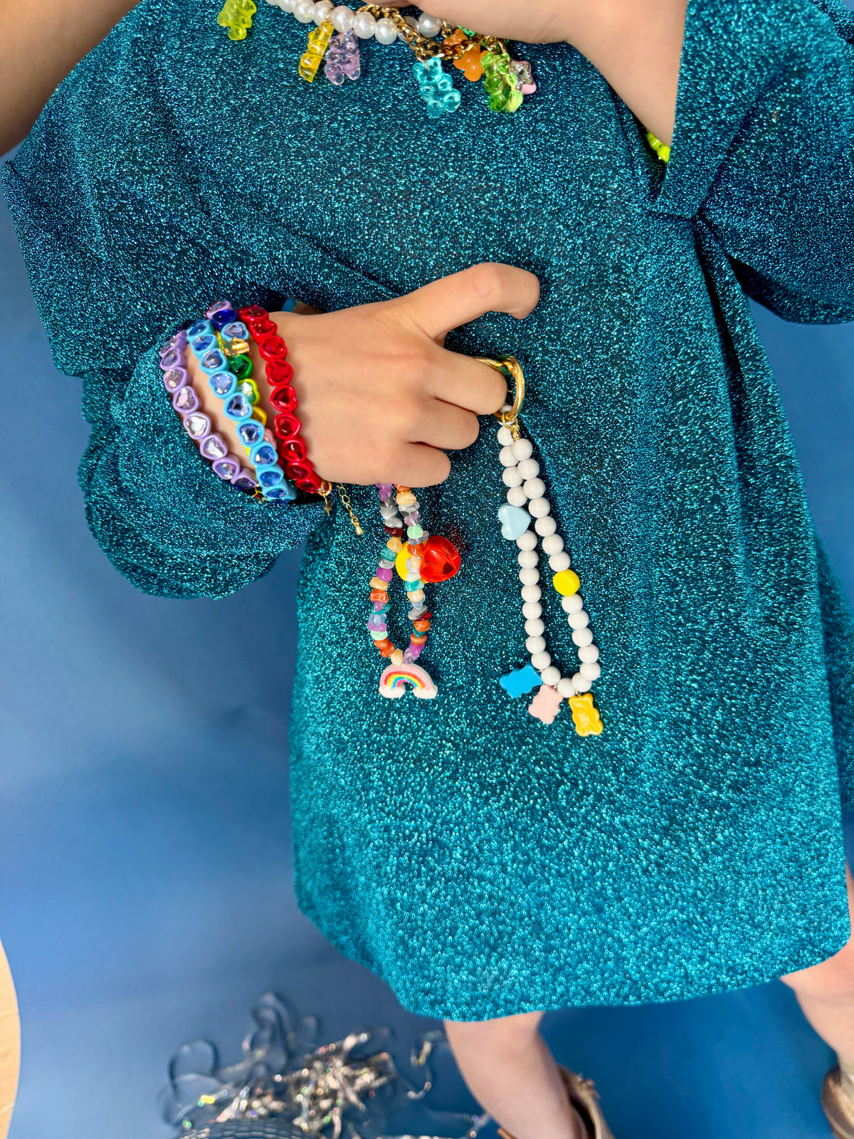 Person wearing colorful bracelets and holding a beaded necklace against a blue background