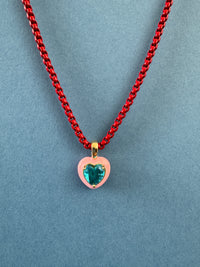 Necklace with a red chain and pink pendant featuring a blue gemstone on a blue background