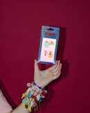 Hand holding a package labeled 'roger' against a red background. box of charms with cat, pineapple, heart and omg charm