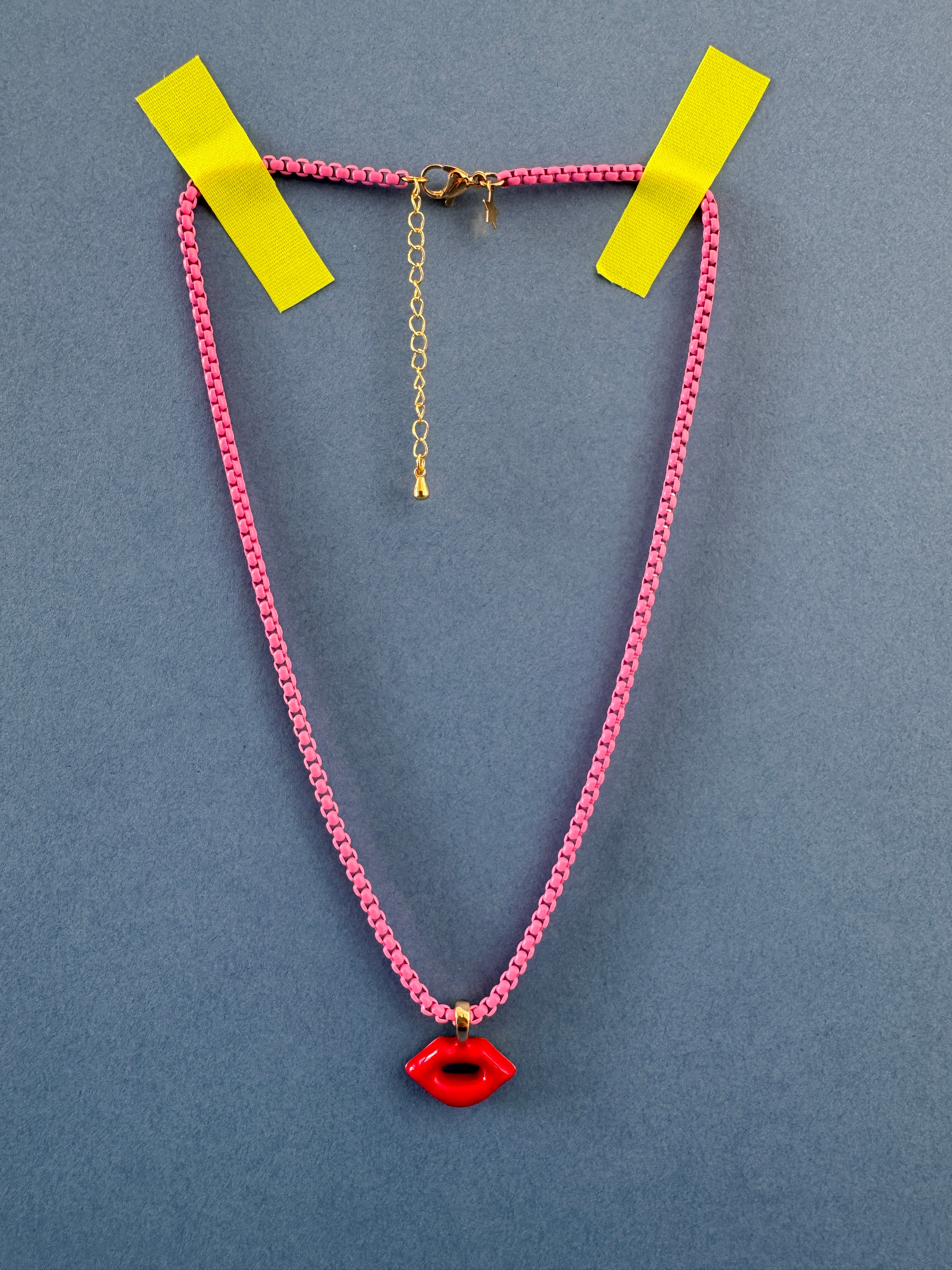 Necklace with pink chain, gold clasp, and red pendant on a gray background