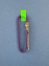 Purple chain bracelet with gold clasp on a gray background
