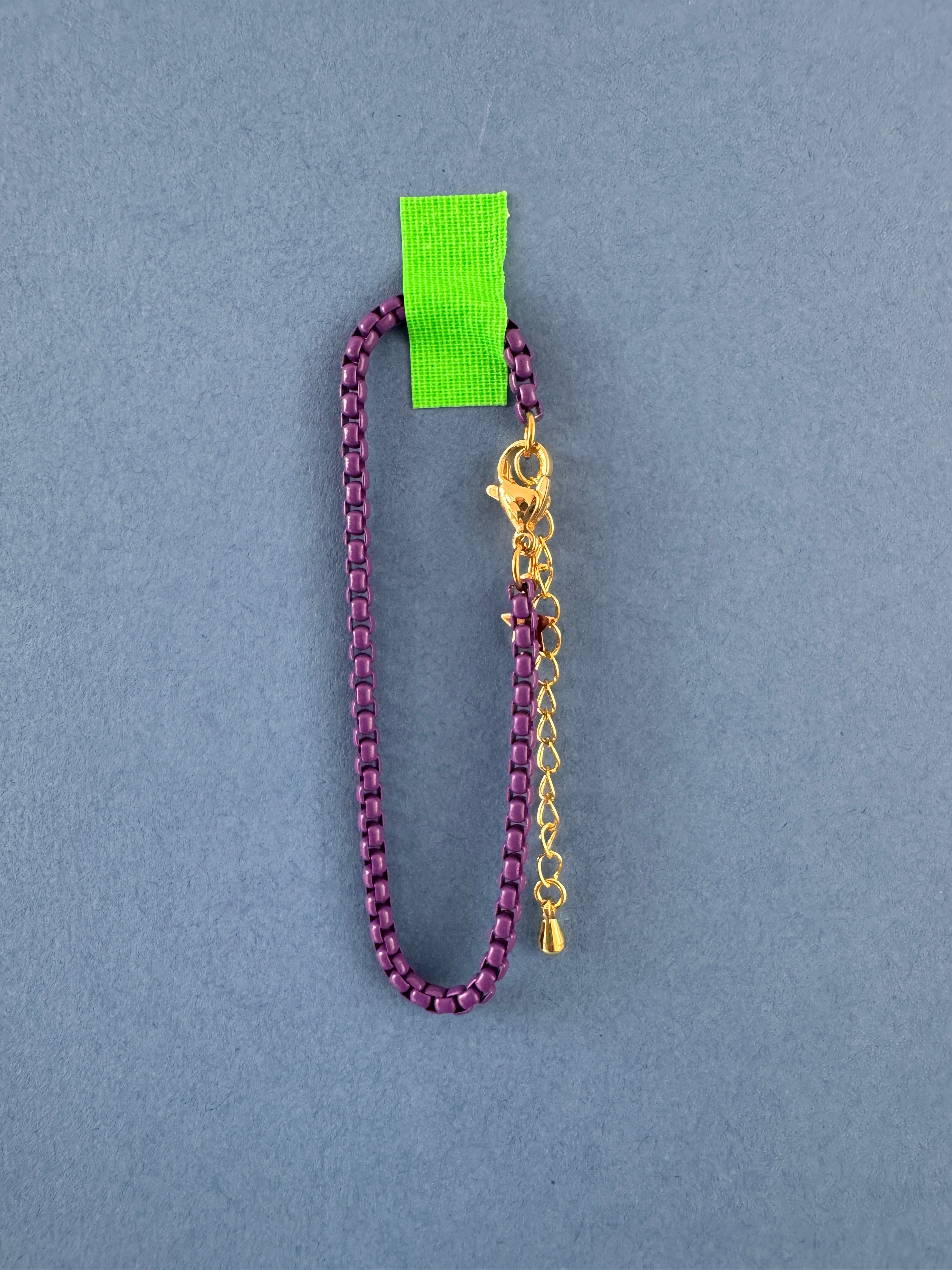 Purple chain bracelet with gold clasp on a gray background