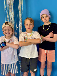 Three children posing against a blue background with decorative streamers.