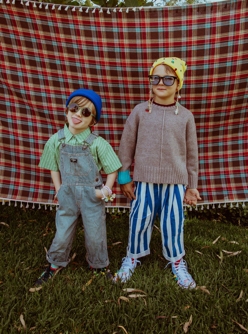 Two children standing in front of a plaid blanket on grass