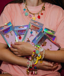 A person holding boxes of sneaker charms with various designs such as cherries, hearts, and bananas, and wearing matching roger charms for jewellery.