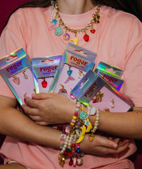 A person holding boxes of sneaker charms with various designs such as cherries, hearts, and bananas, and wearing matching roger charms for jewellery.