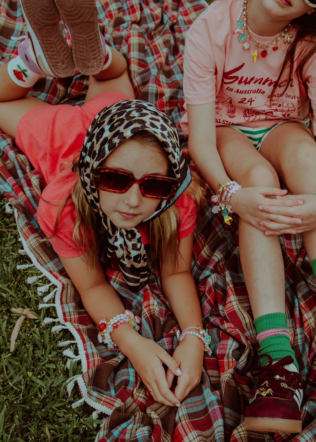 Girls sitting outside on blanket wearing Roger Pearl Power sneaker charms on bracelets.