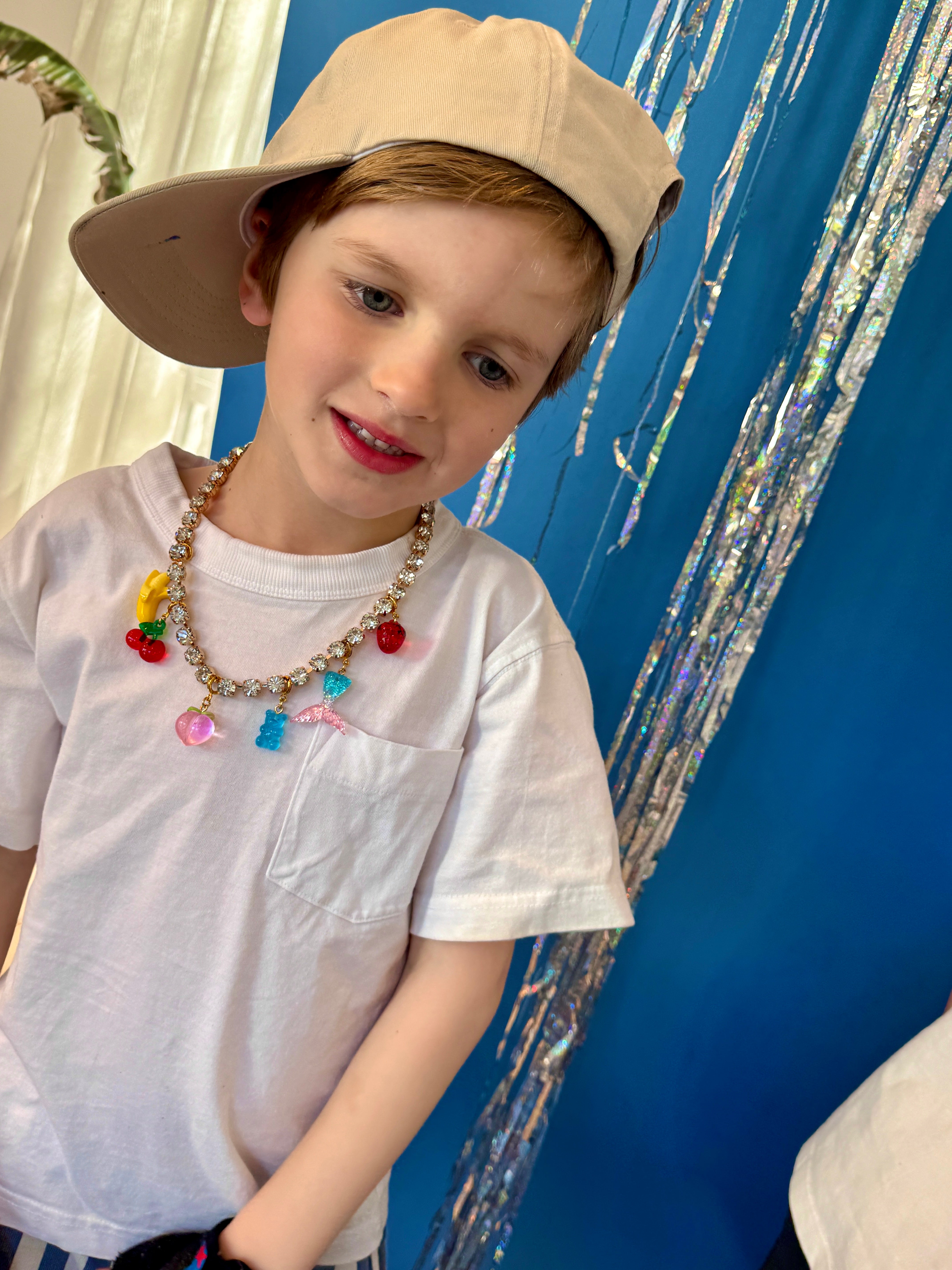 Child wearing a beige cap and colorful necklace against a blue background with decorative elements.