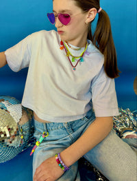 girl wearing colourful sunglasses and multiple necklaces, sitting with a disco ball against a blue background
