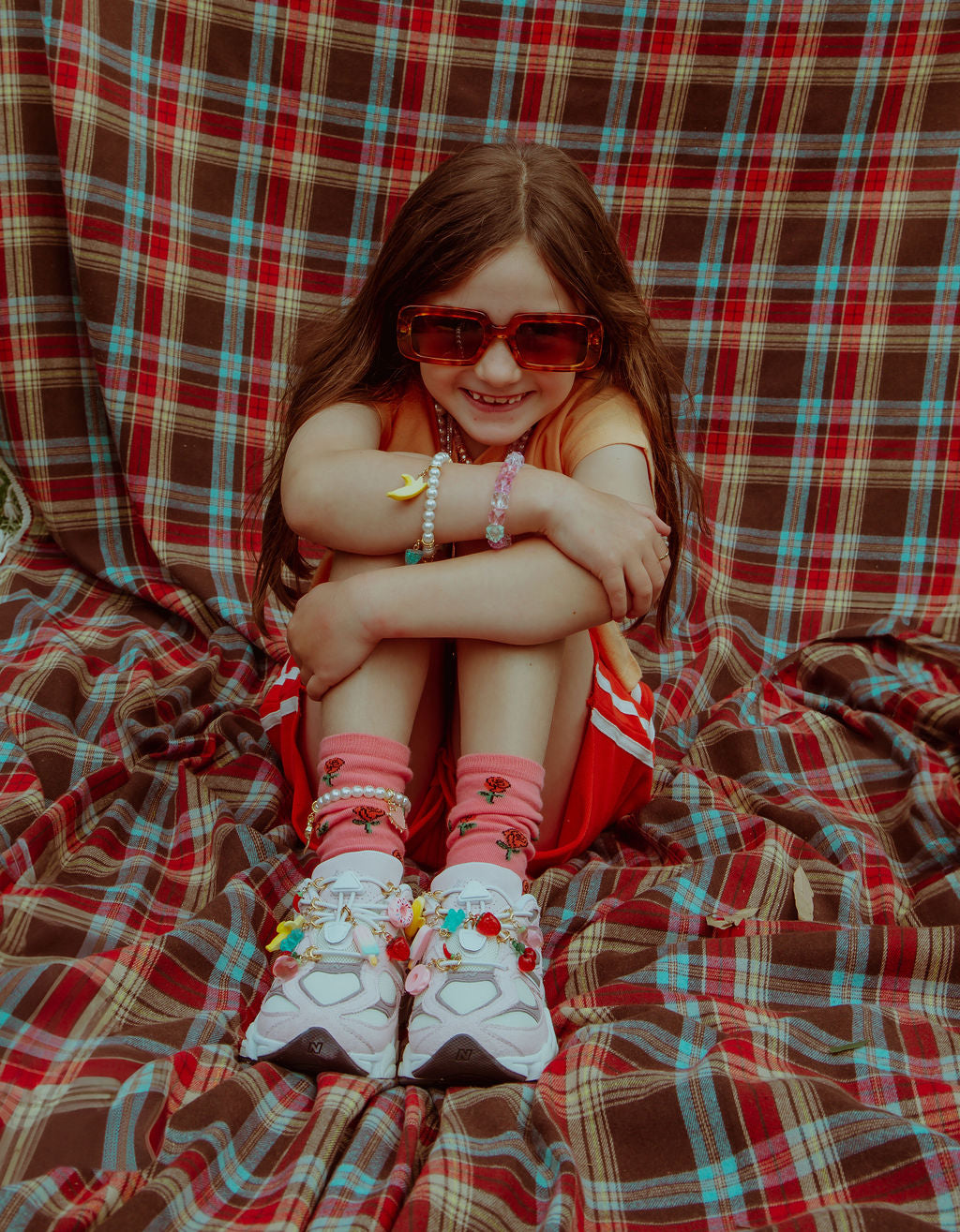 Girl on blanket smiling with Roger Official sneaker charms. Super cool shoe bling.