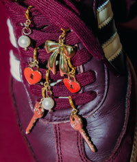 Extra close image of sneaker charms on shoes. Gold bow charm, heart charm, key charm and pearl charm