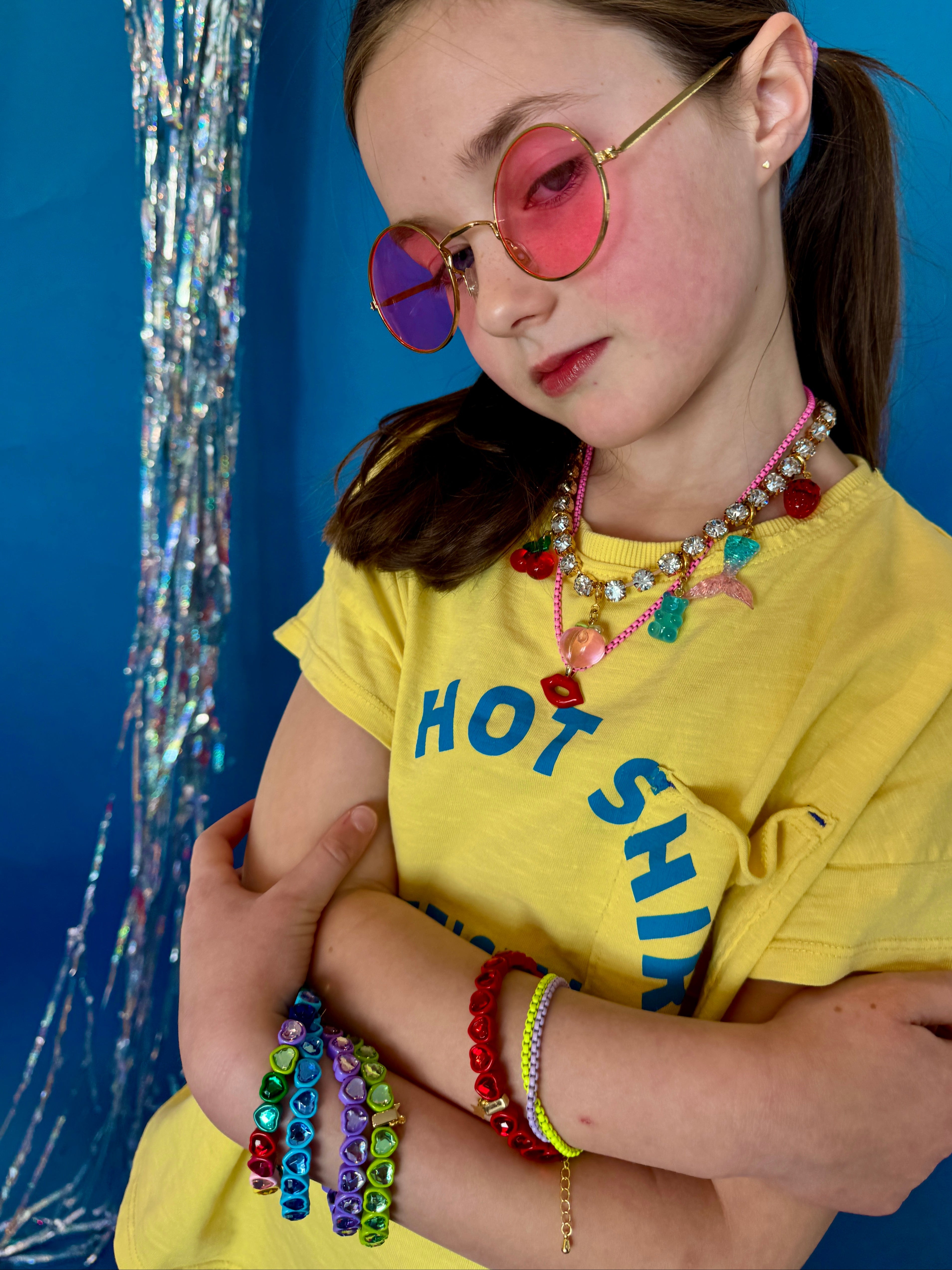 Young girl wearing colorful sunglasses and multiple necklaces with a blue background