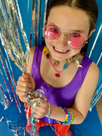 Young girl in a purple top with colorful accessories holding streamers against a blue background