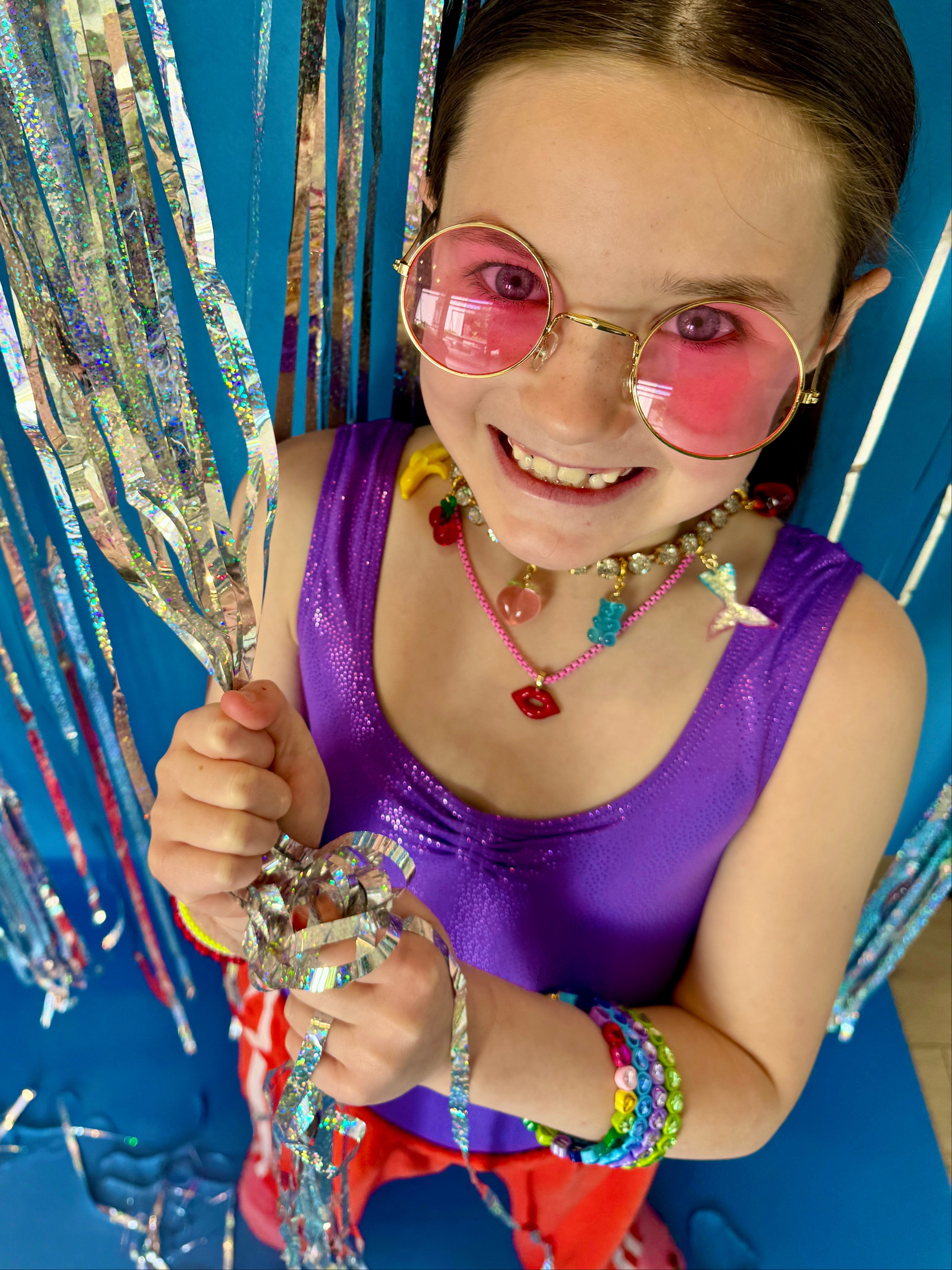Young girl in a purple top with colorful accessories holding streamers against a blue background