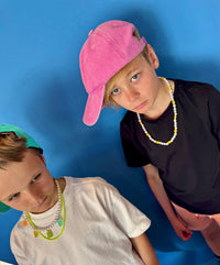Two children wearing colorful hats and necklaces against a blue background